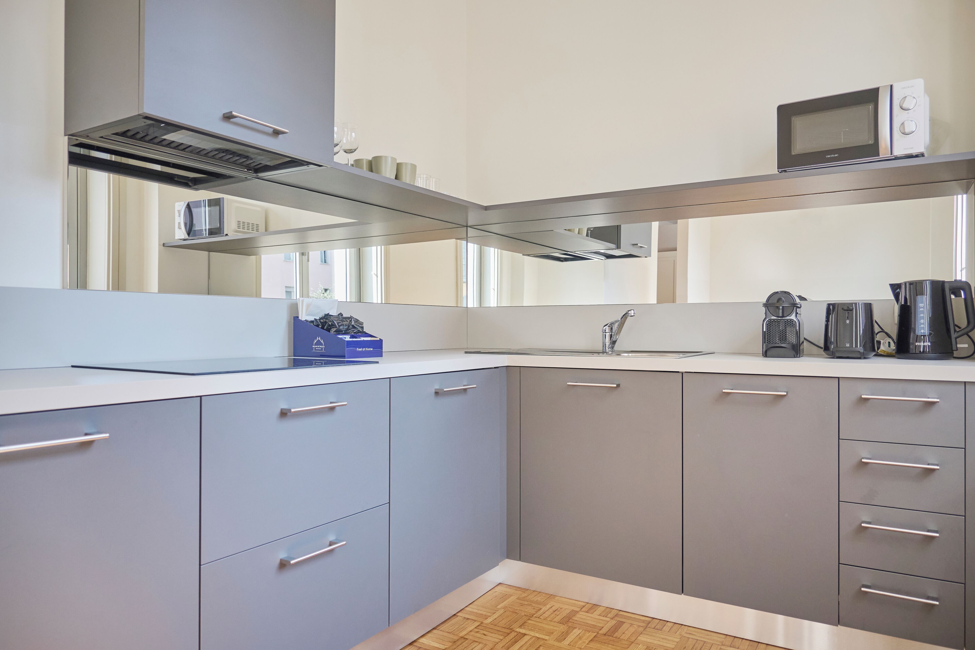 Una cucina moderna con mobili grigi, una cappa aspirante in acciaio inossidabile, un forno a microonde e una macchina da caffè.