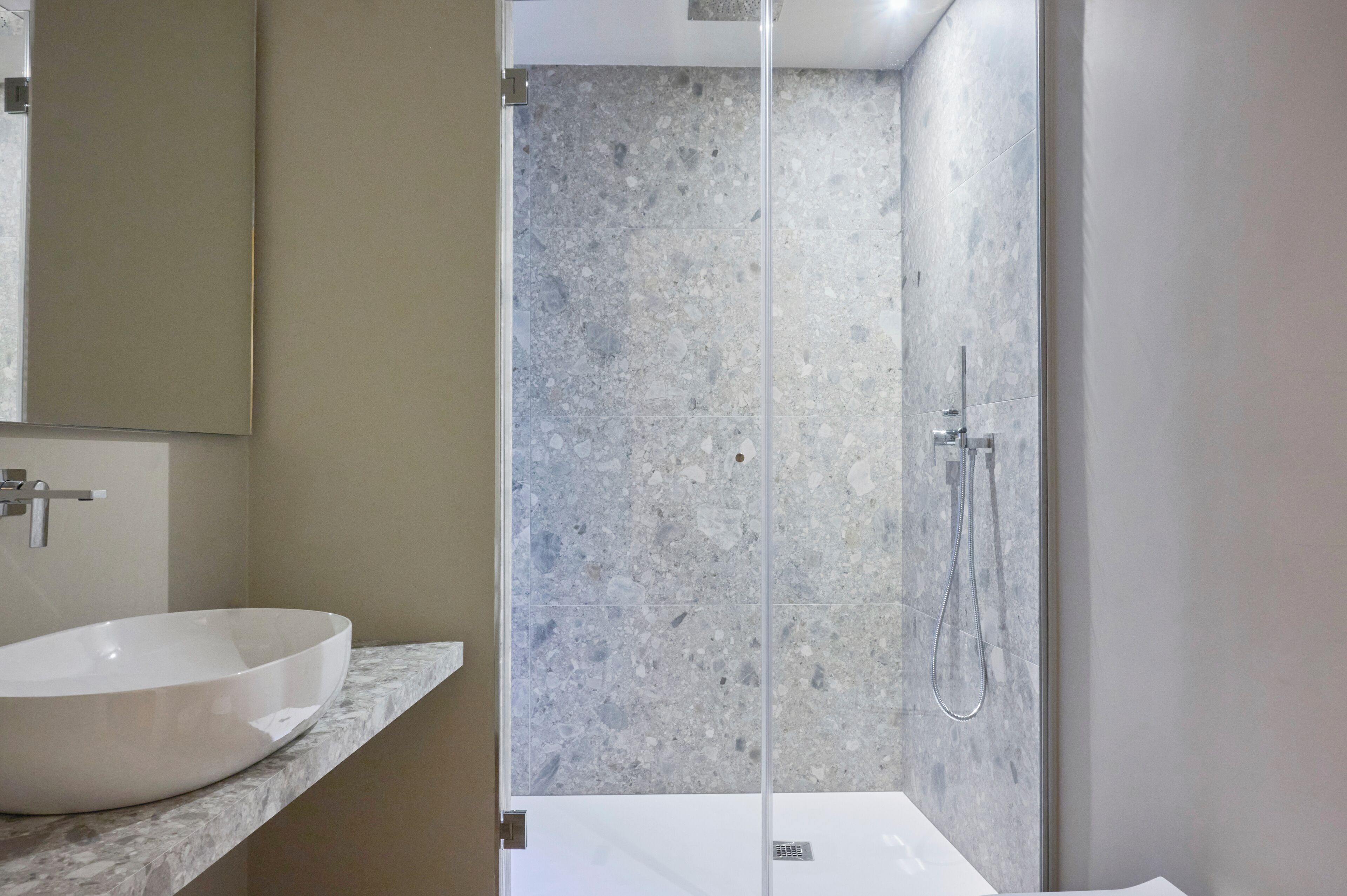 A modern bathroom with a large white sink, a glass shower enclosure, and a marble-tiled shower area.