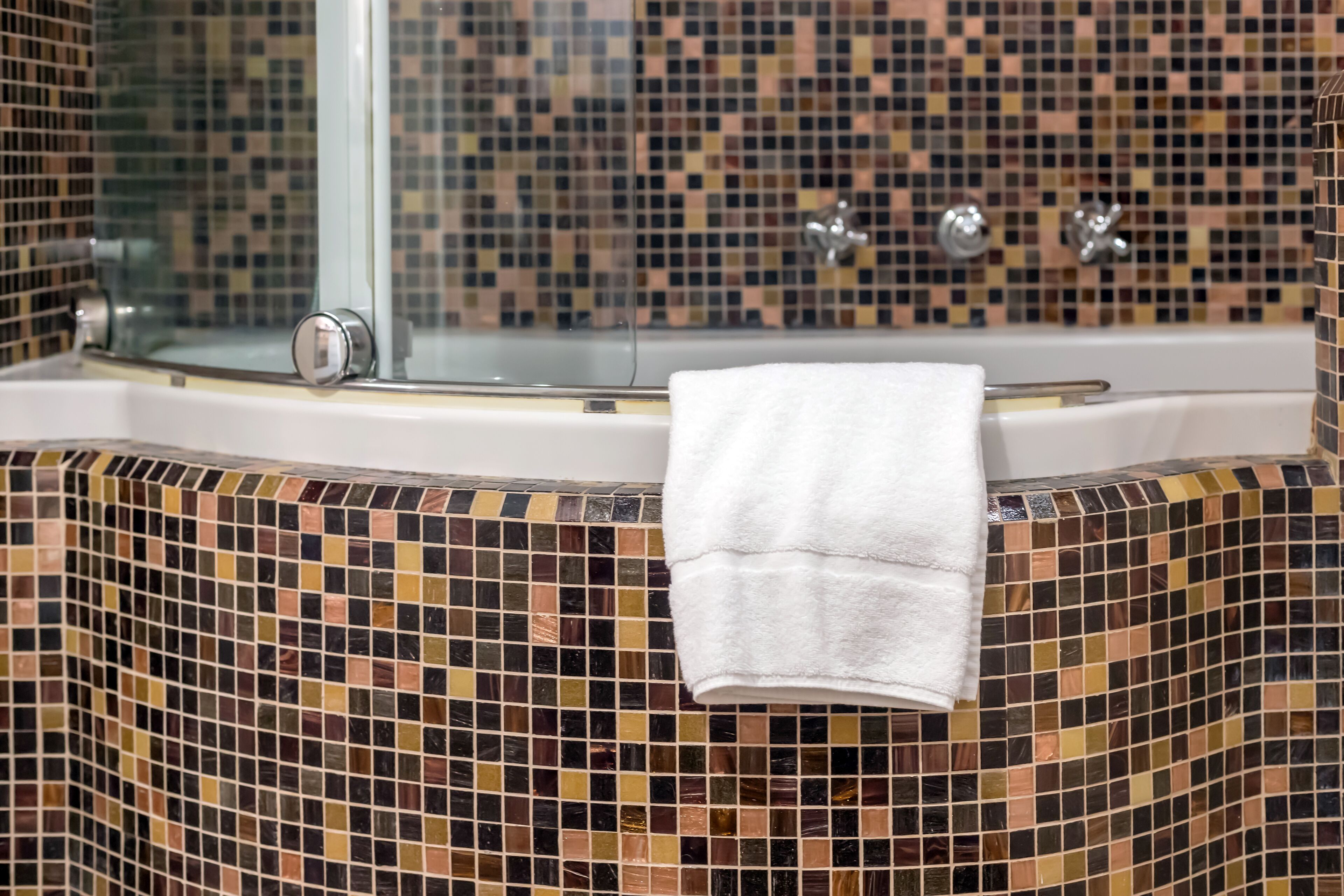 Une salle de bain avec un mur recouvert de mosaïques, une douche en verre et une serviette blanche accrochée au mur.