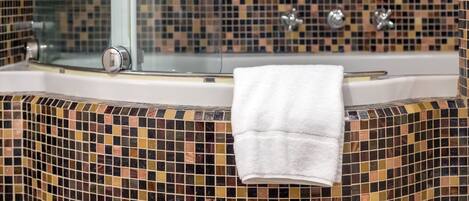 Une salle de bain avec un mur recouvert de mosaïques, une douche en verre et une serviette blanche accrochée au mur.