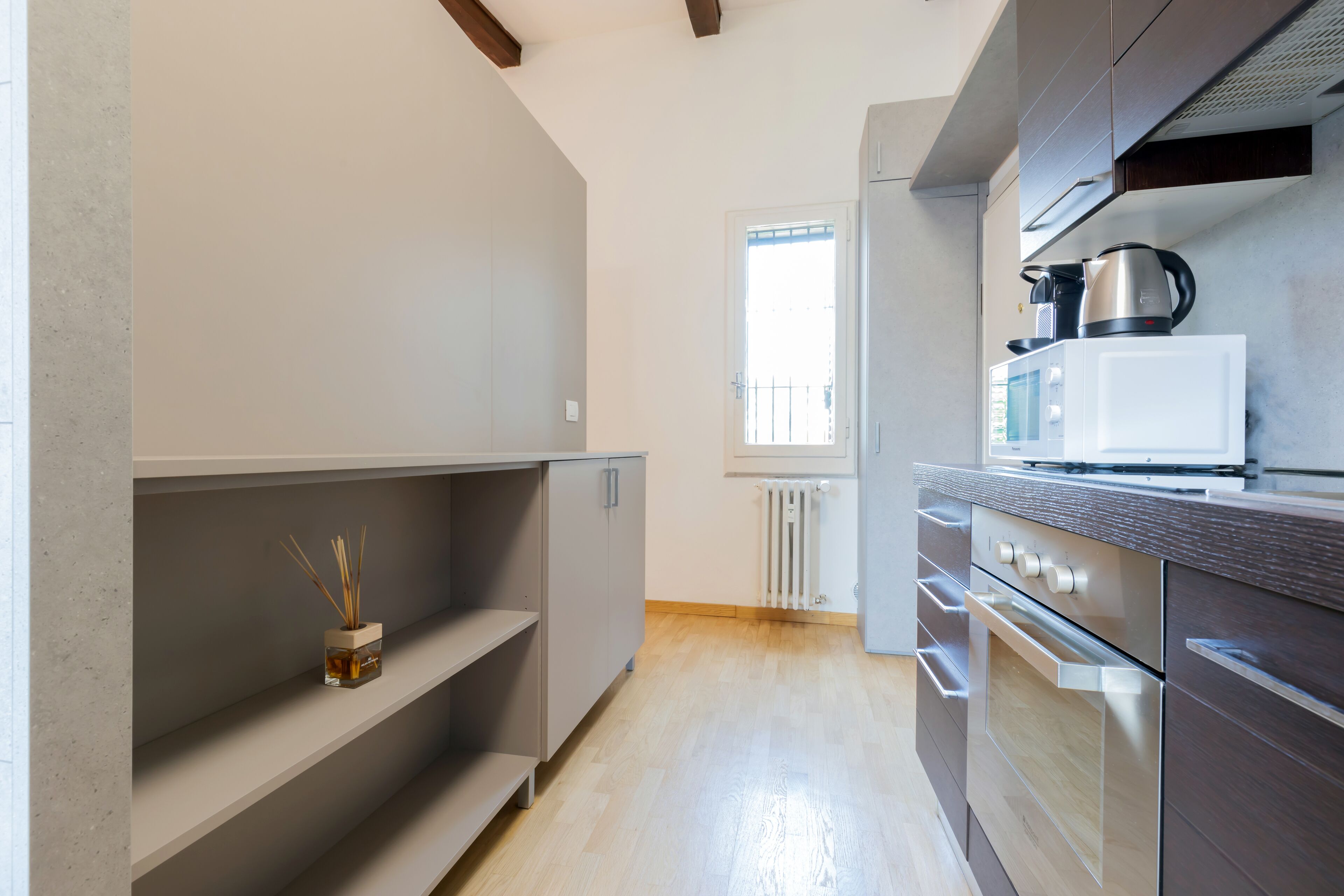 A modern kitchen with built-in appliances, wooden flooring, and a window with a view.