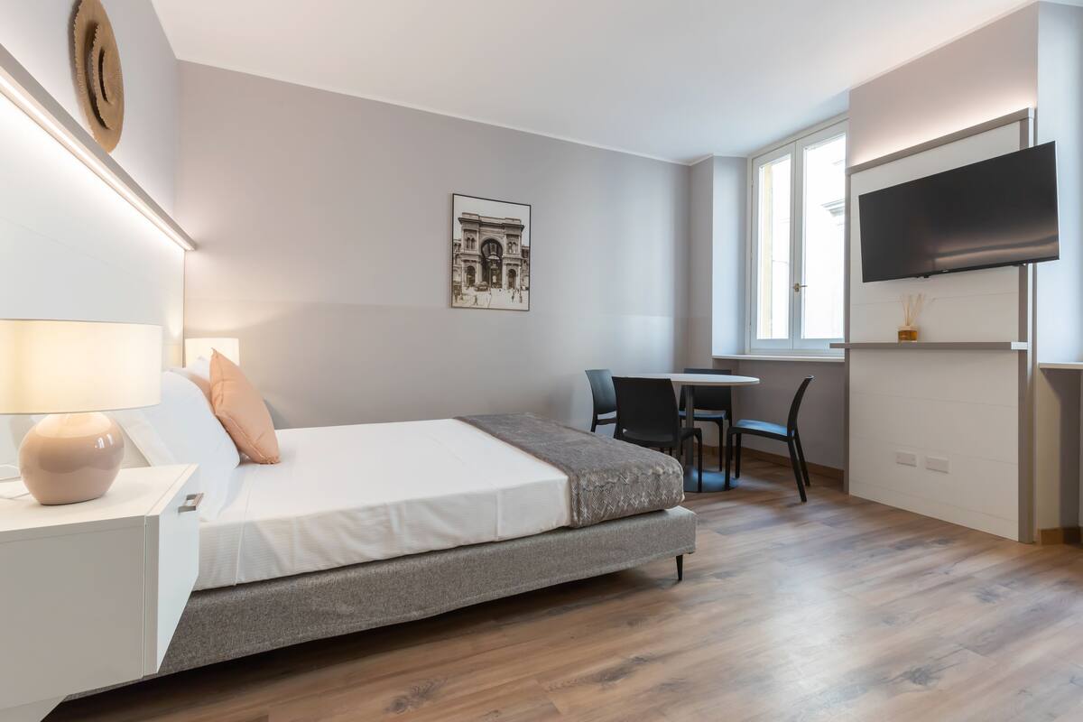 Un dormitorio moderno con cama, mesita de noche, lámpara y televisor instalado en la pared.