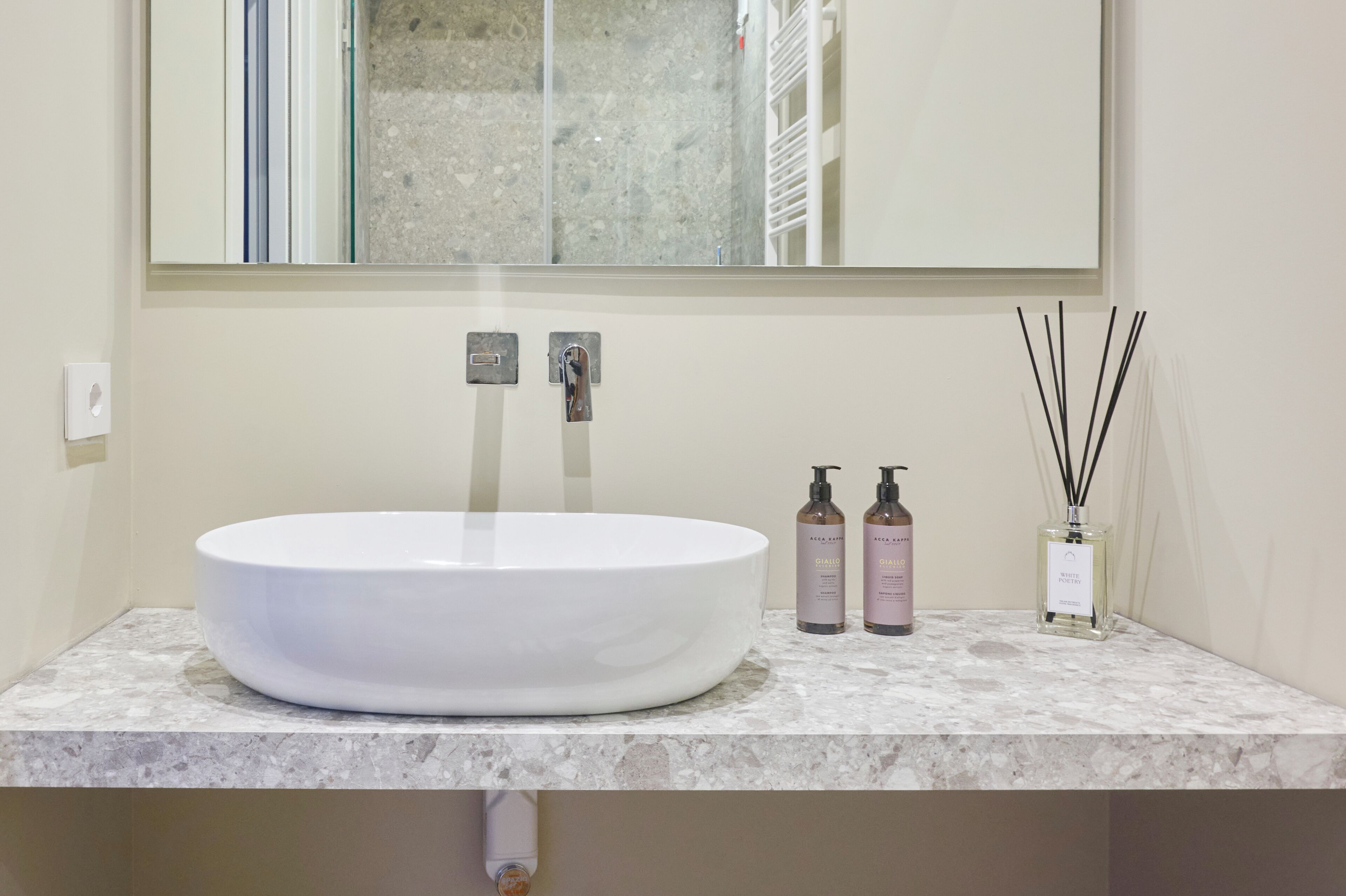 A bathroom with a white sink, two soap dispensers, and a reed diffuser on the countertop.