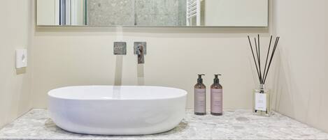 A bathroom with a white sink, two soap dispensers, and a reed diffuser on the countertop.