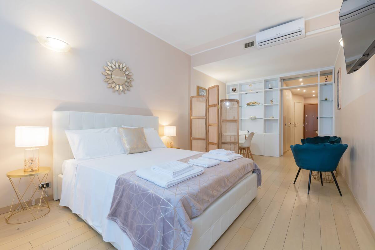 Una habitación de hotel con una cama grande, mesitas de noche, una silla y un armario.