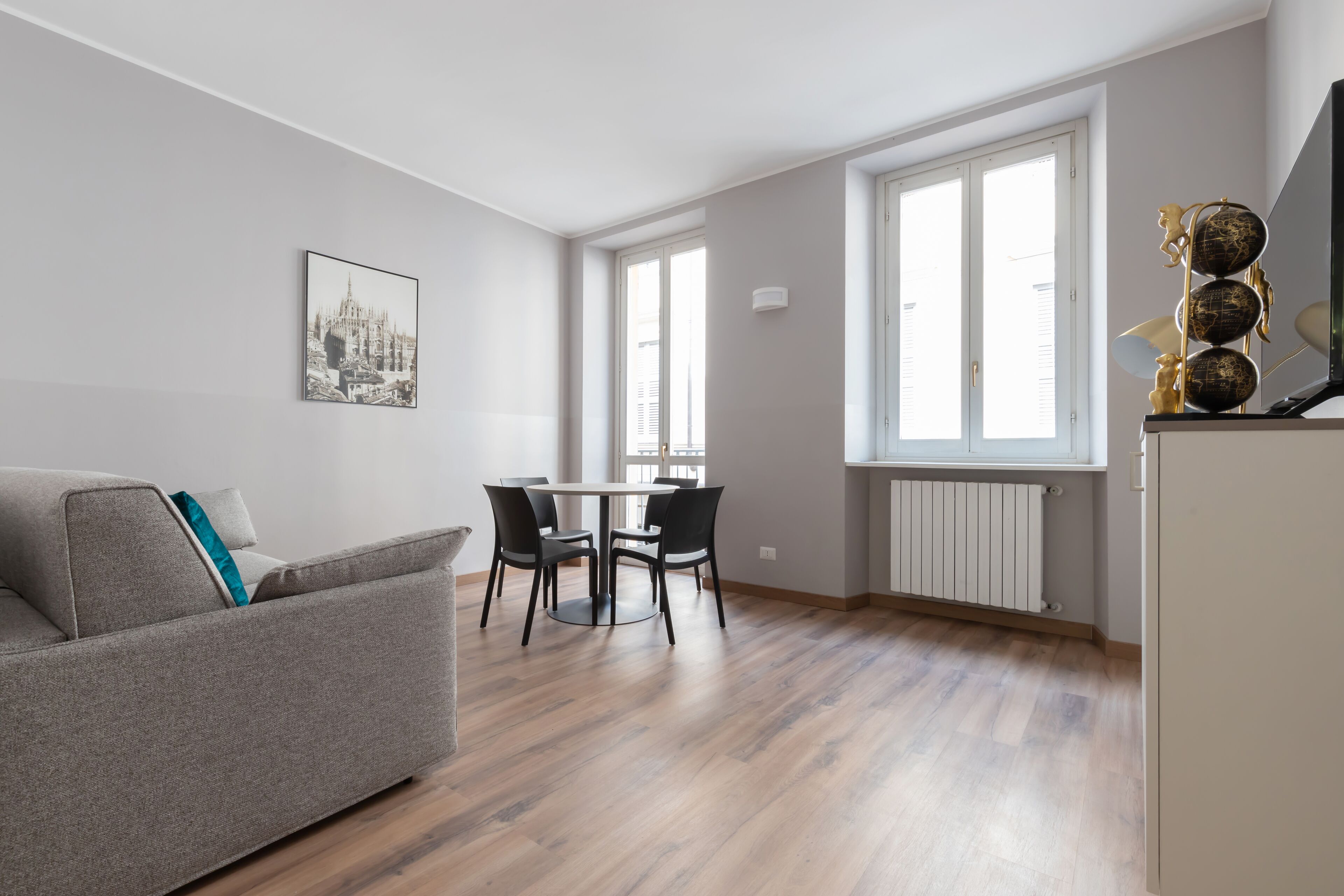 Una sala de estar moderna con un sofá gris, una mesa de comedor con cuatro sillas y un amplio ventanal que proporciona luz natural.