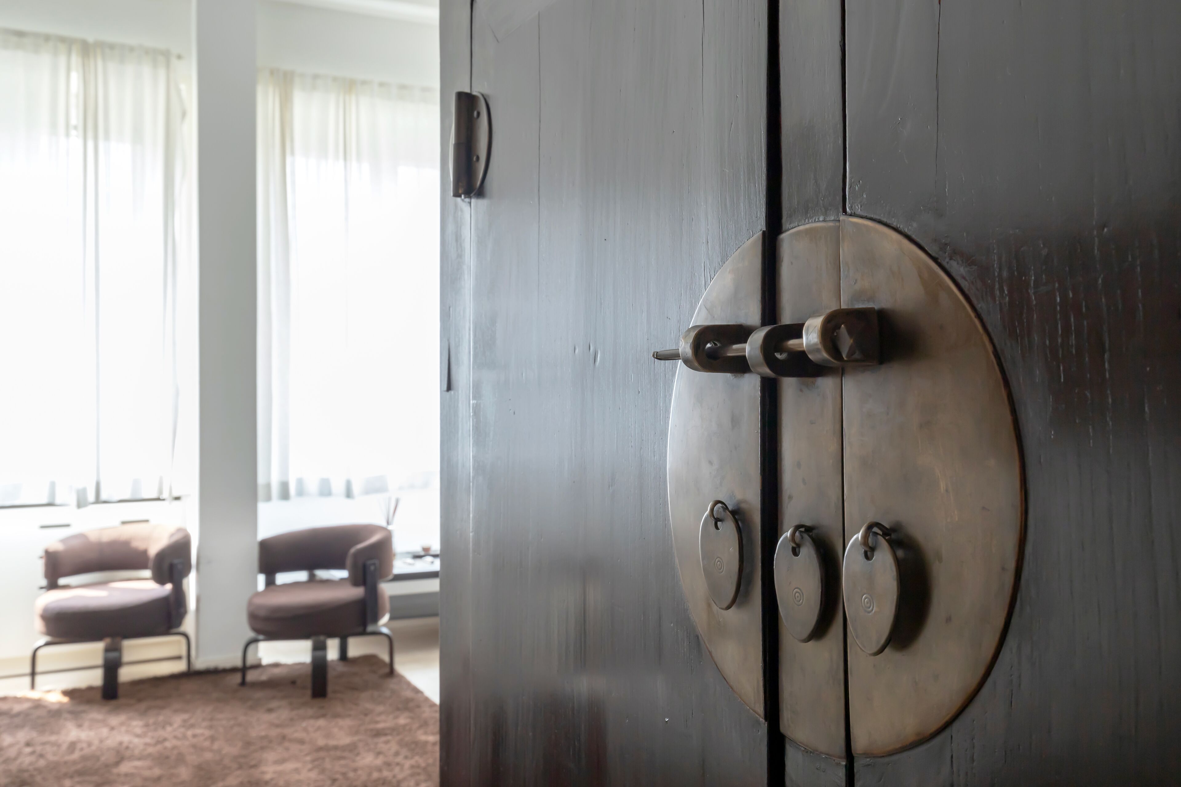 Ein Zimmer mit einer großen Holztür, zwei runden Metallgriffen und einem Fenster mit durchsichtigen Vorhängen.