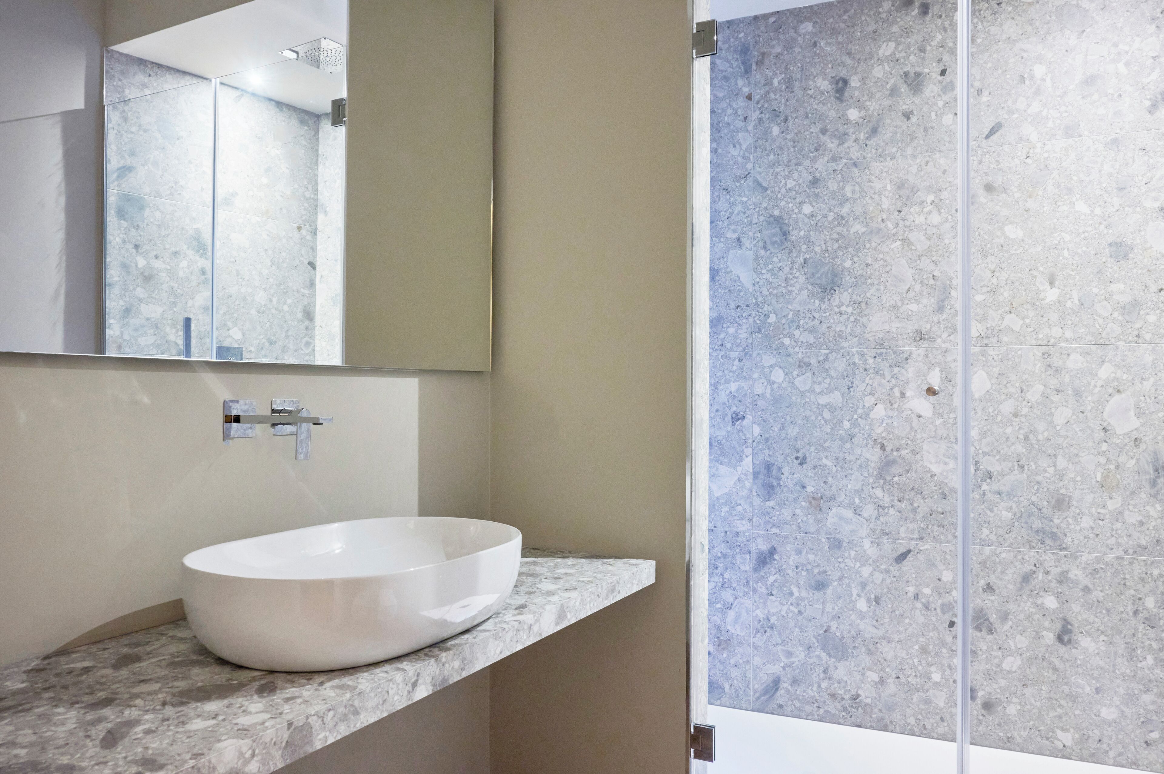 A bathroom with a white vessel sink, a mirror, and a shower with a speckled tile wall.