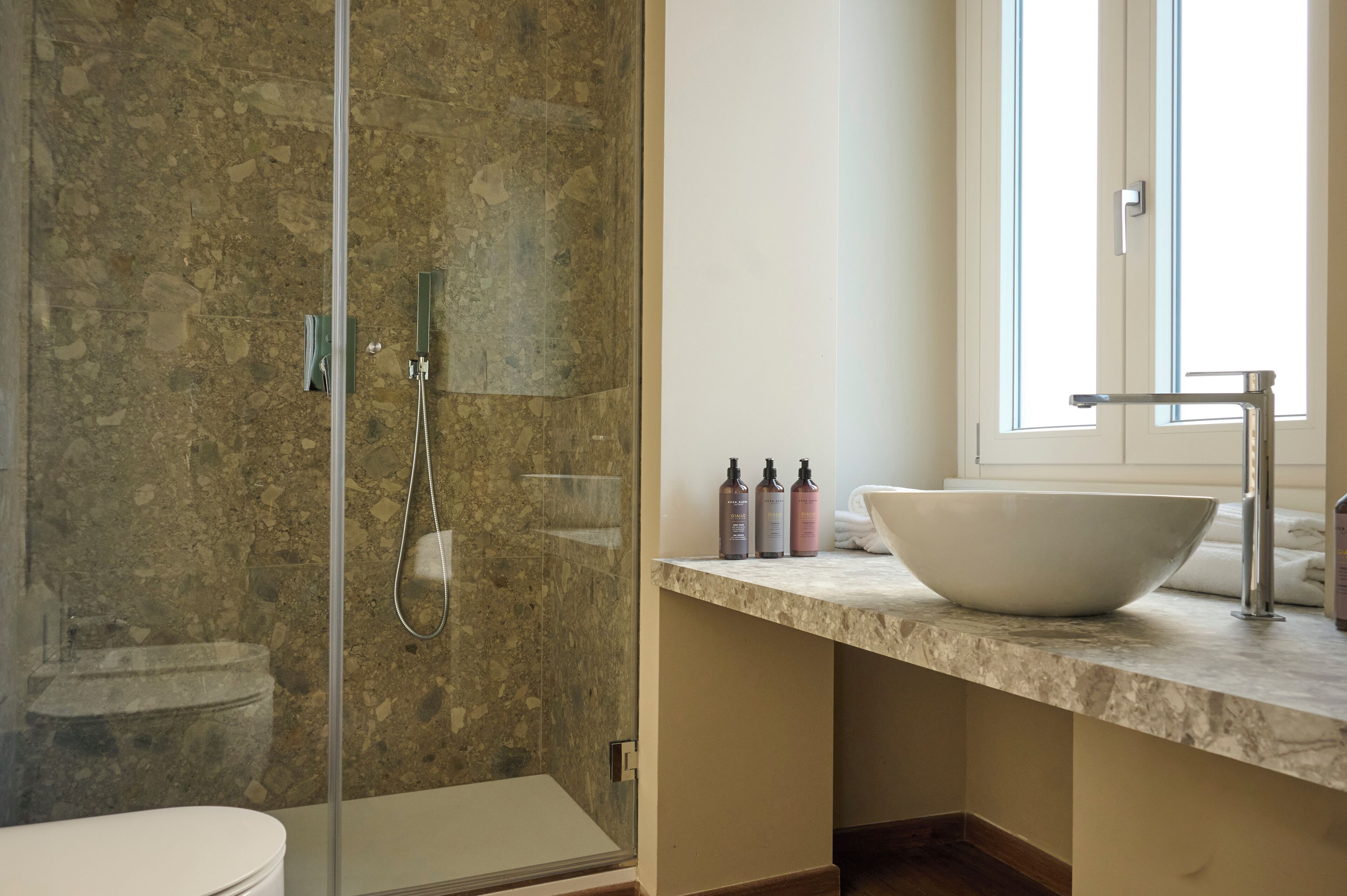 A bathroom with a glass-enclosed shower, a white sink, and a window.
