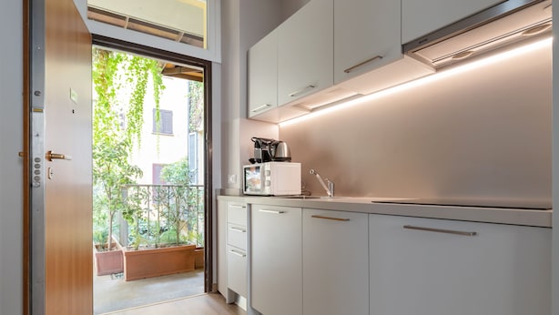 Una cocina moderna con armarios blancos, una cafetera y vistas a un balcón con plantas.