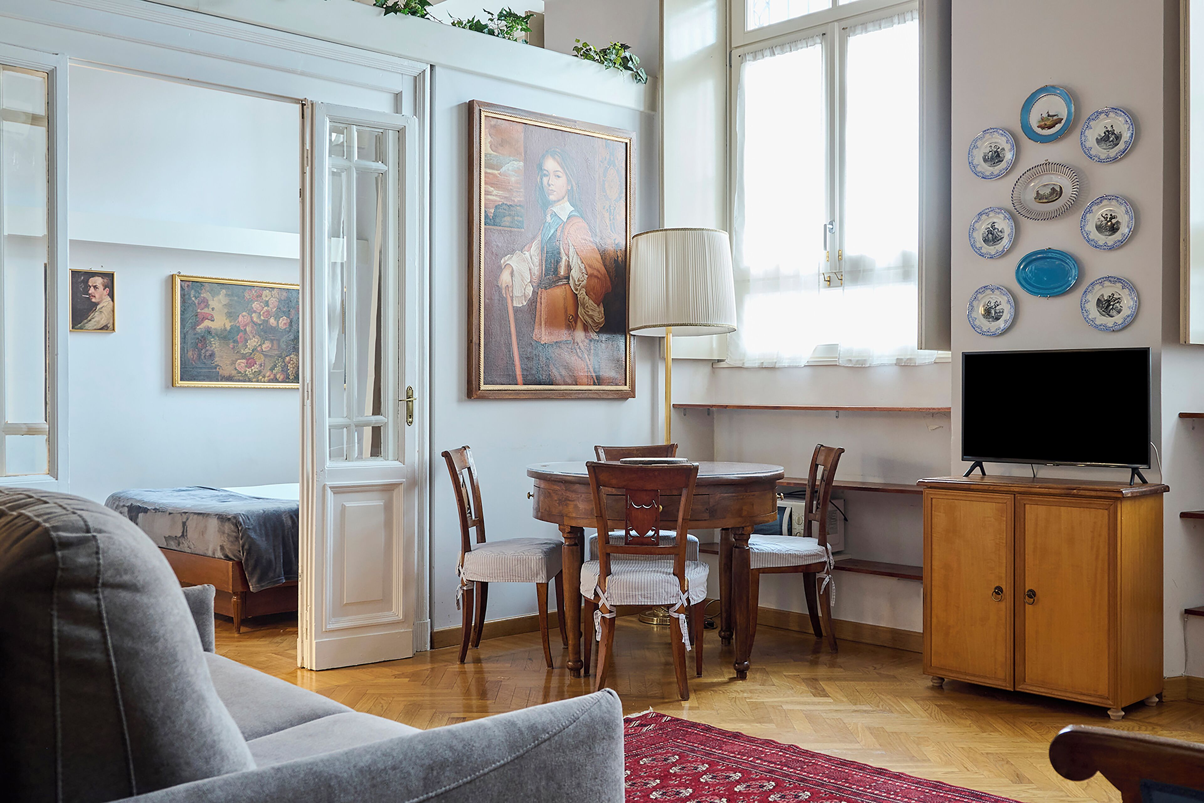 A living room with a sofa, a dining table with chairs, a TV on a wooden cabinet, and a painting on the wall.