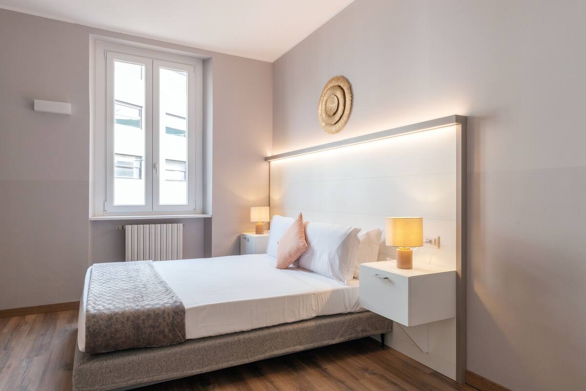Un dormitorio moderno con cama, lámparas de noche, una ventana y un adorno circular en la pared.