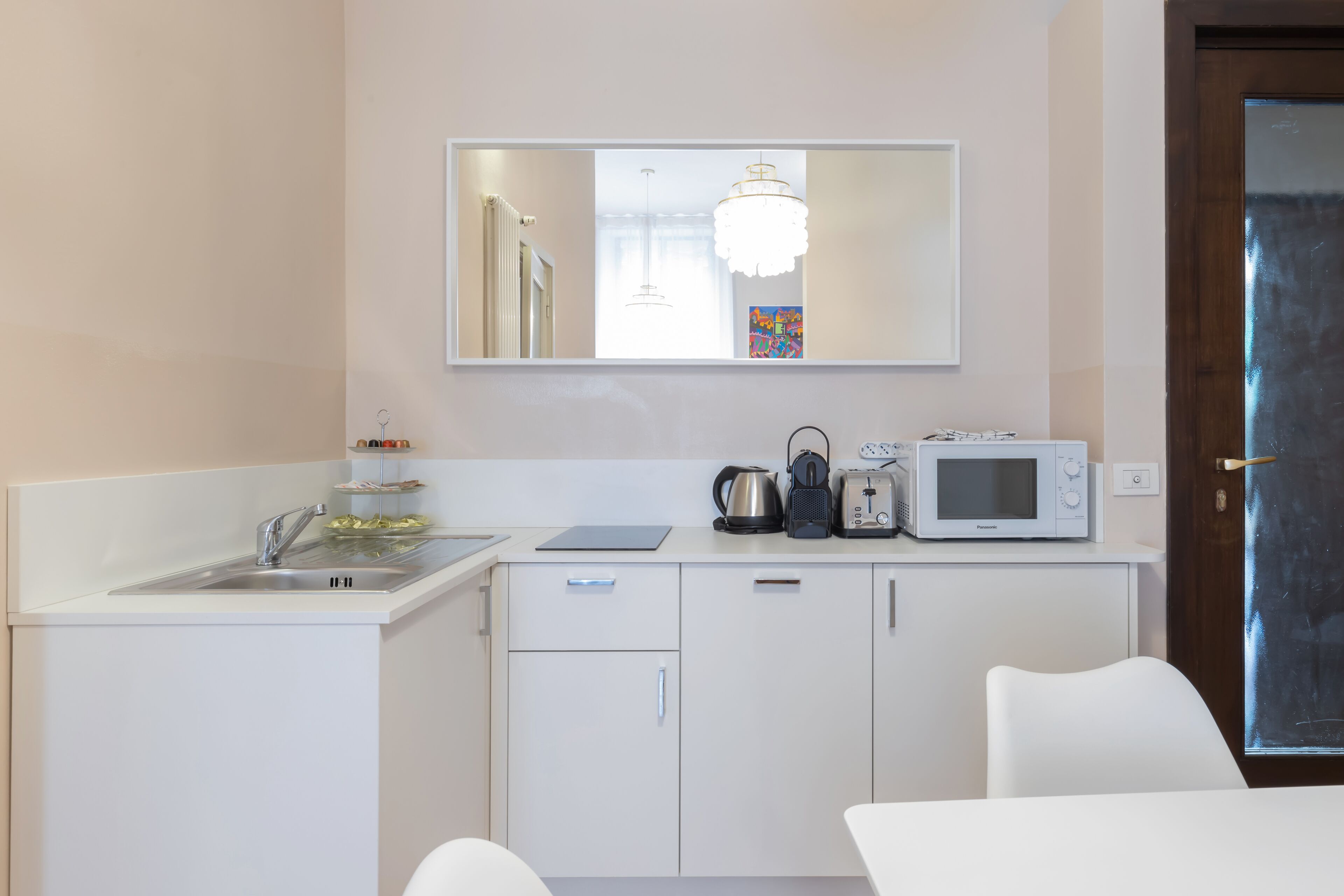 Una kitchenette compacta con lavamanos, microondas, hervidor, tostadora y una pequeña encimera.