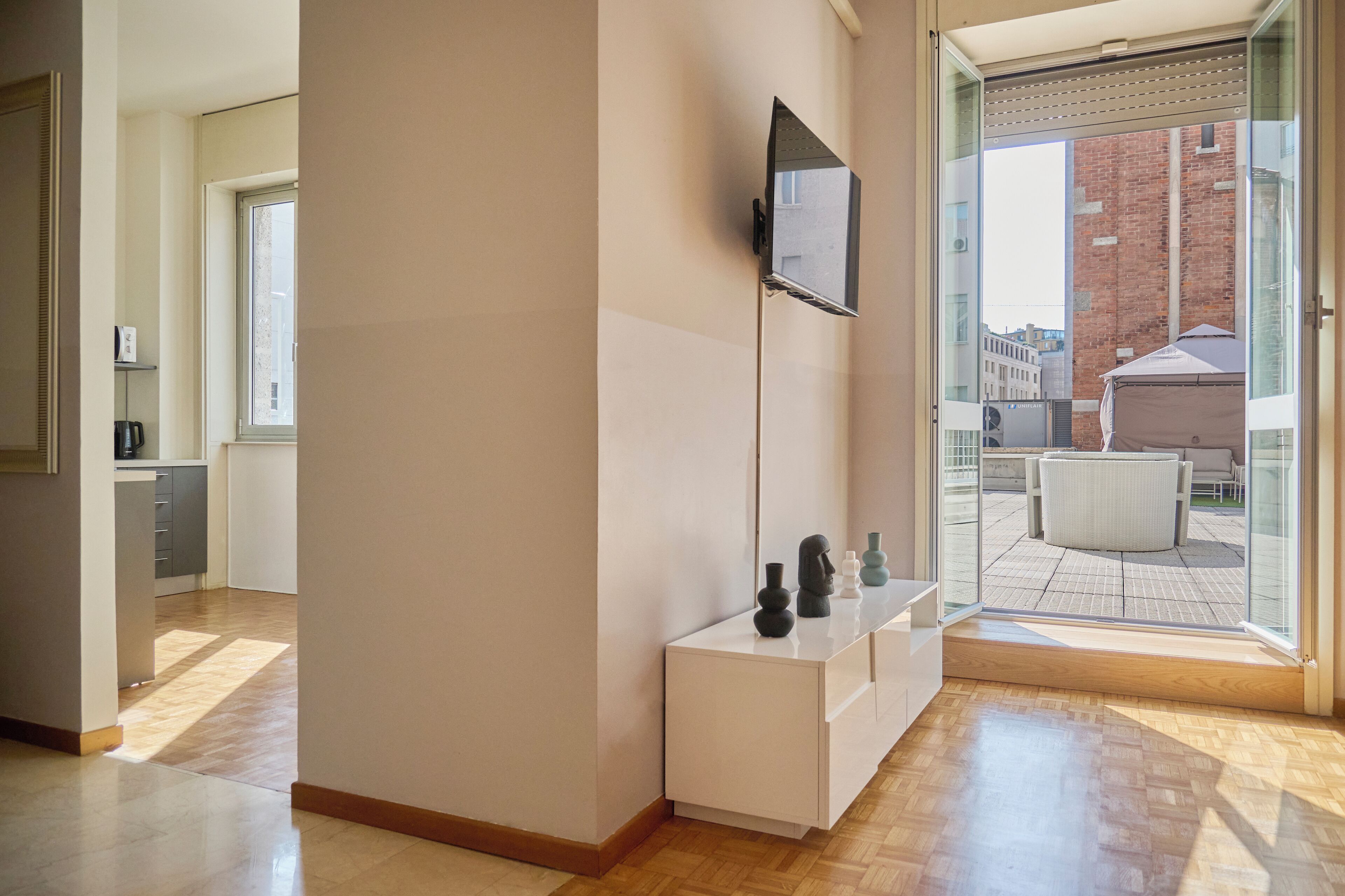 A modern interior with a flat-screen TV mounted on a wall, a white console table, and a view of the city through large glass doors.