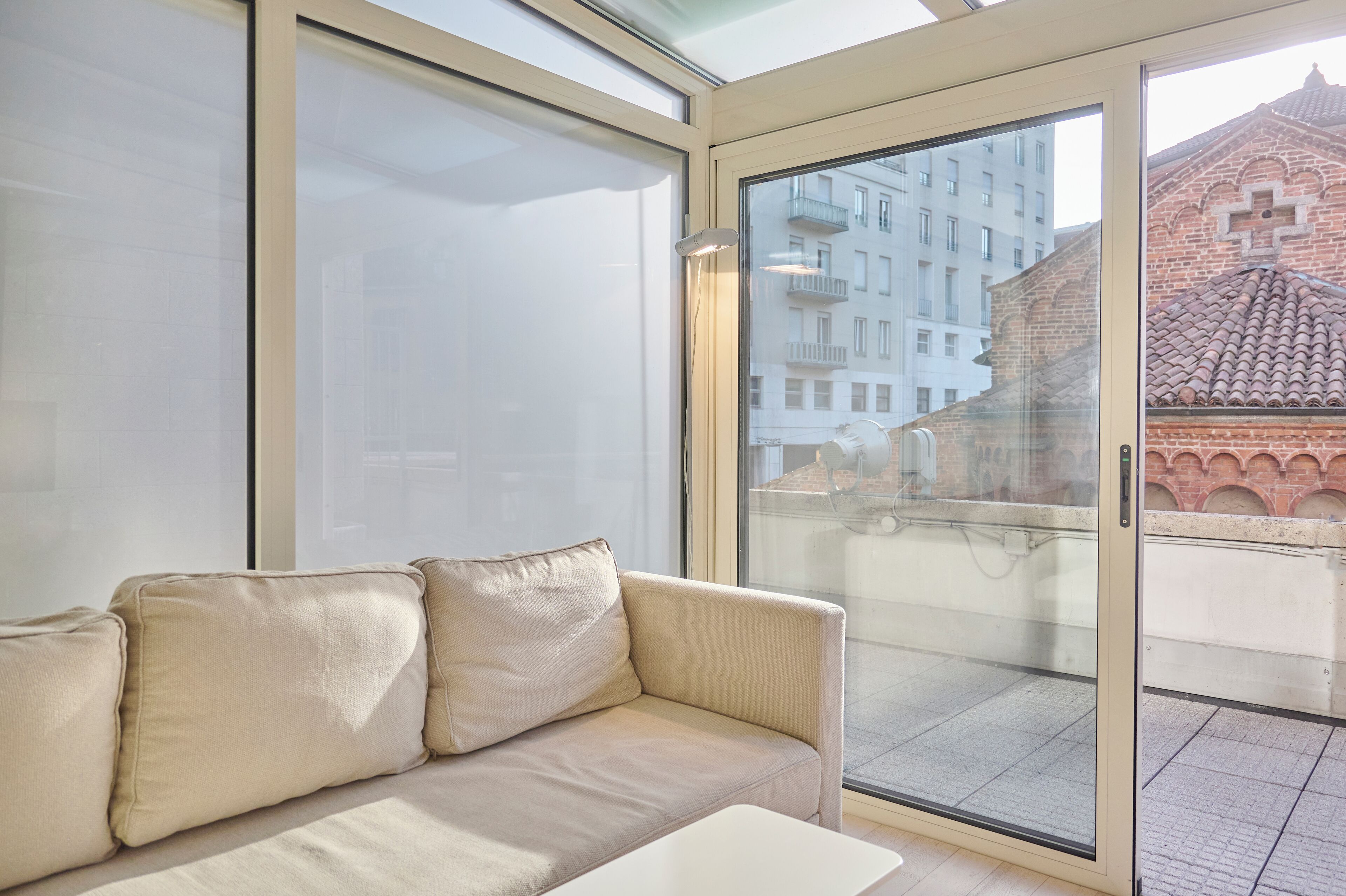 A modern living room with a beige sofa, large windows, and a view of a cityscape.