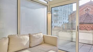 A modern living room with a beige sofa, large windows, and a view of a cityscape.