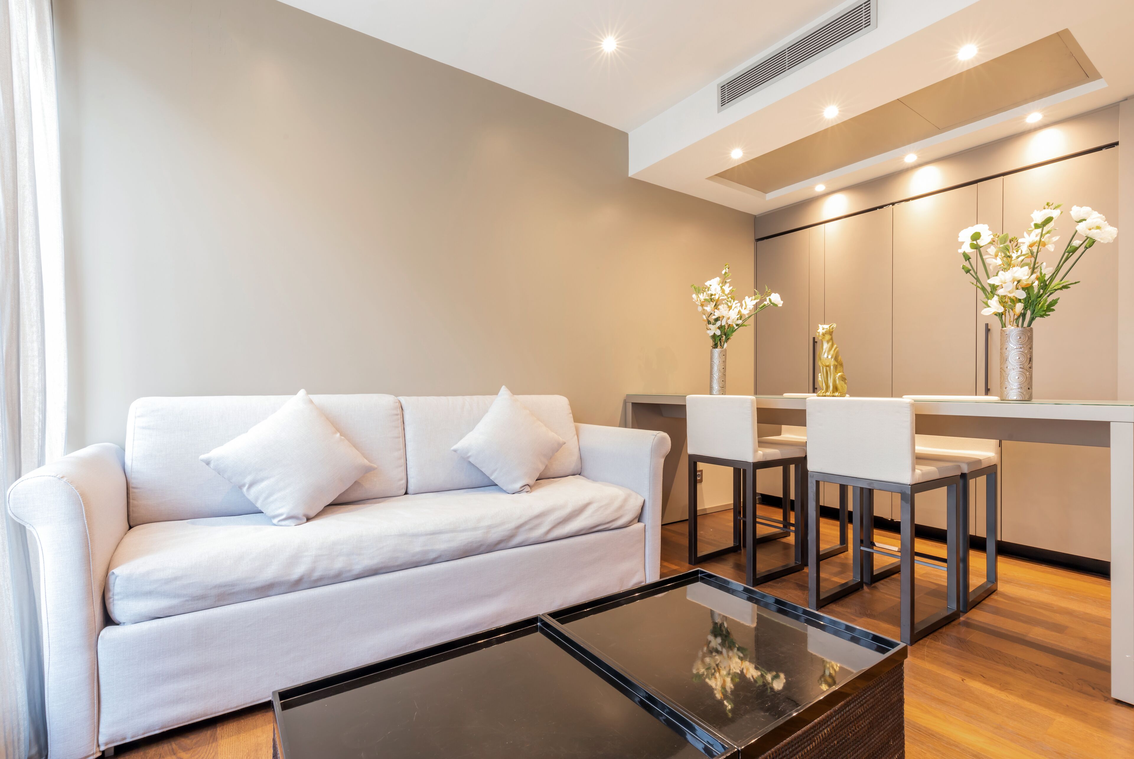 Een moderne woonkamer met een witte bank, een glazen salontafel en een eethoek met stoelen en een bloevas.