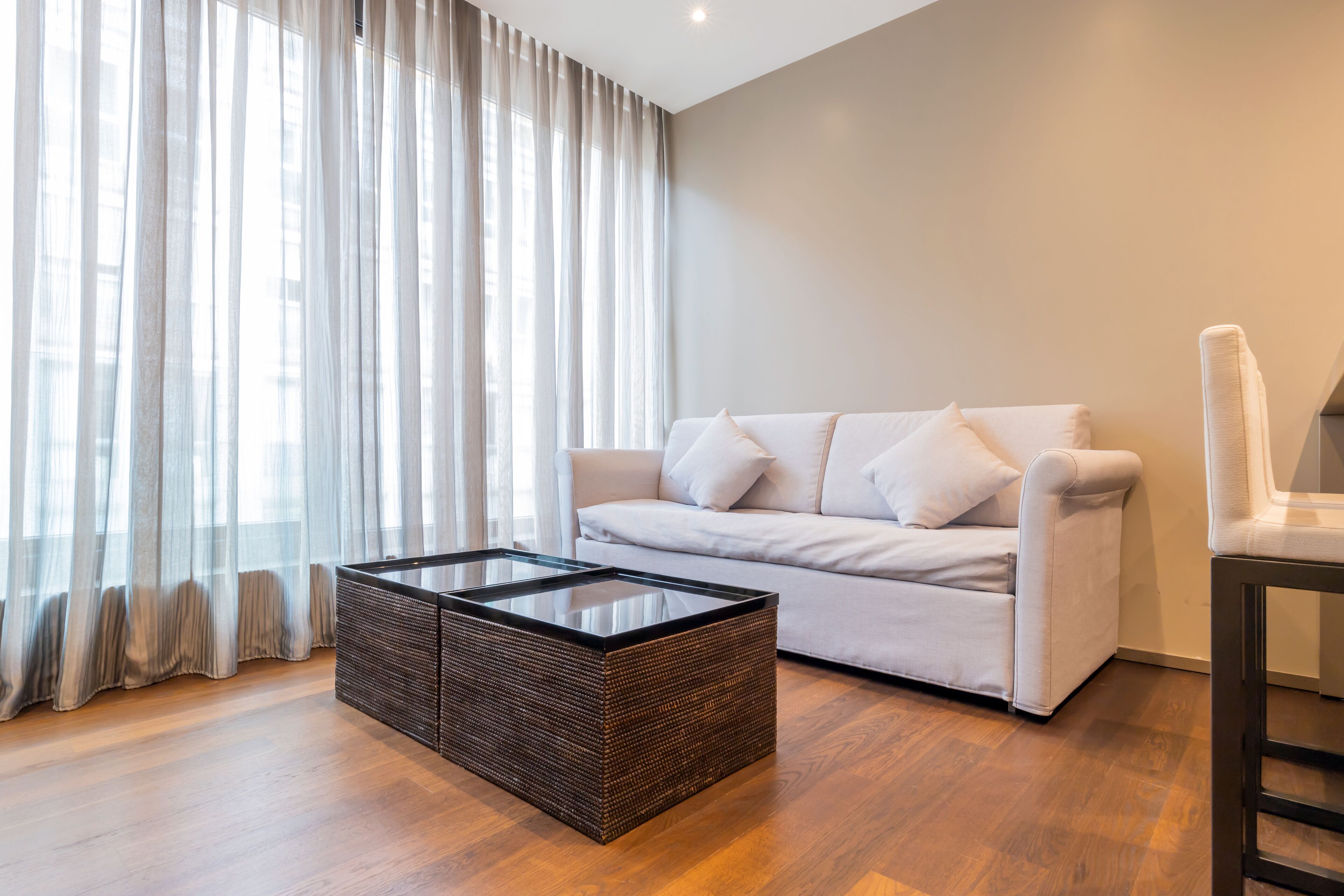 A modern living room with a white sofa, a glass-top coffee table, and a chair.