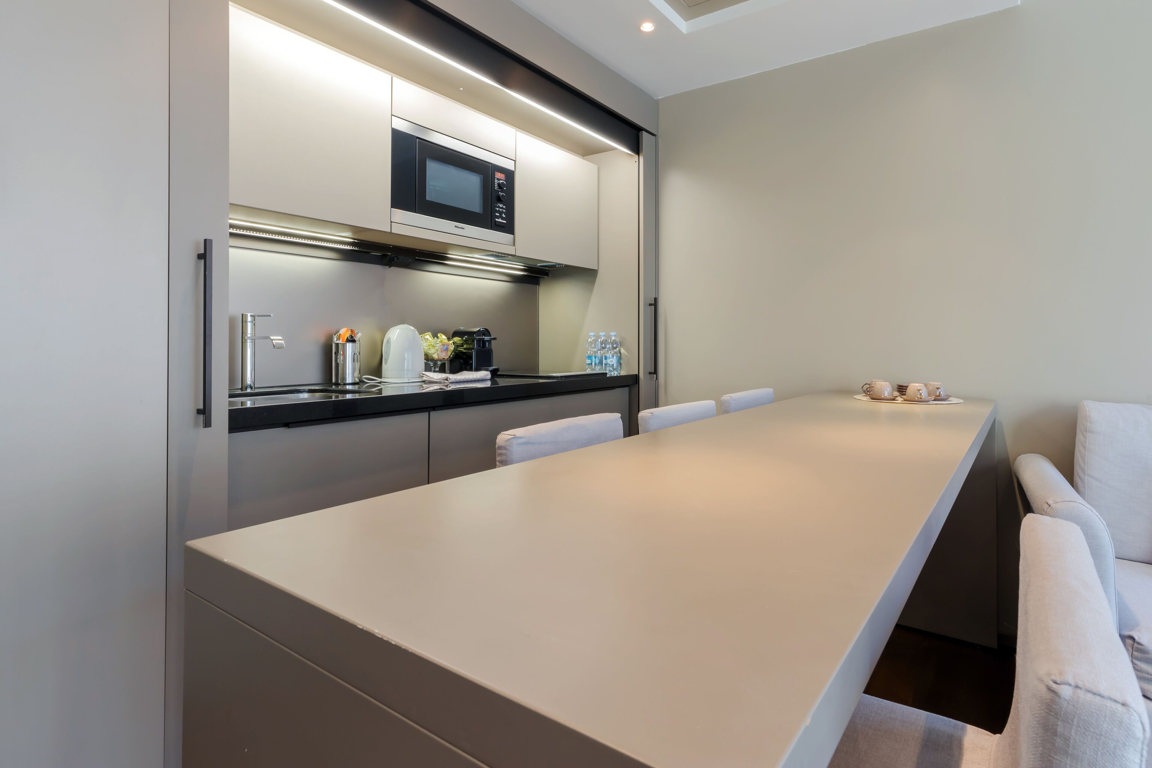 A modern kitchen with a long counter, built-in microwave, and water bottles on the counter.