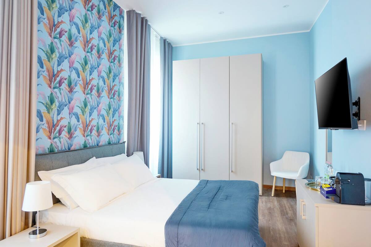 Habitación de hotel con cama, escritorio, silla, televisor y armario.