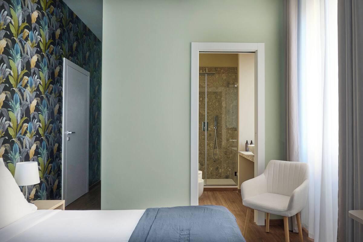 Habitación de hotel con cama, una silla, zona de ducha y baño.