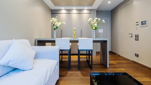 Una habitación de hotel moderna con sofá, una mesa de comedor con sillas y una pequeña cocina.