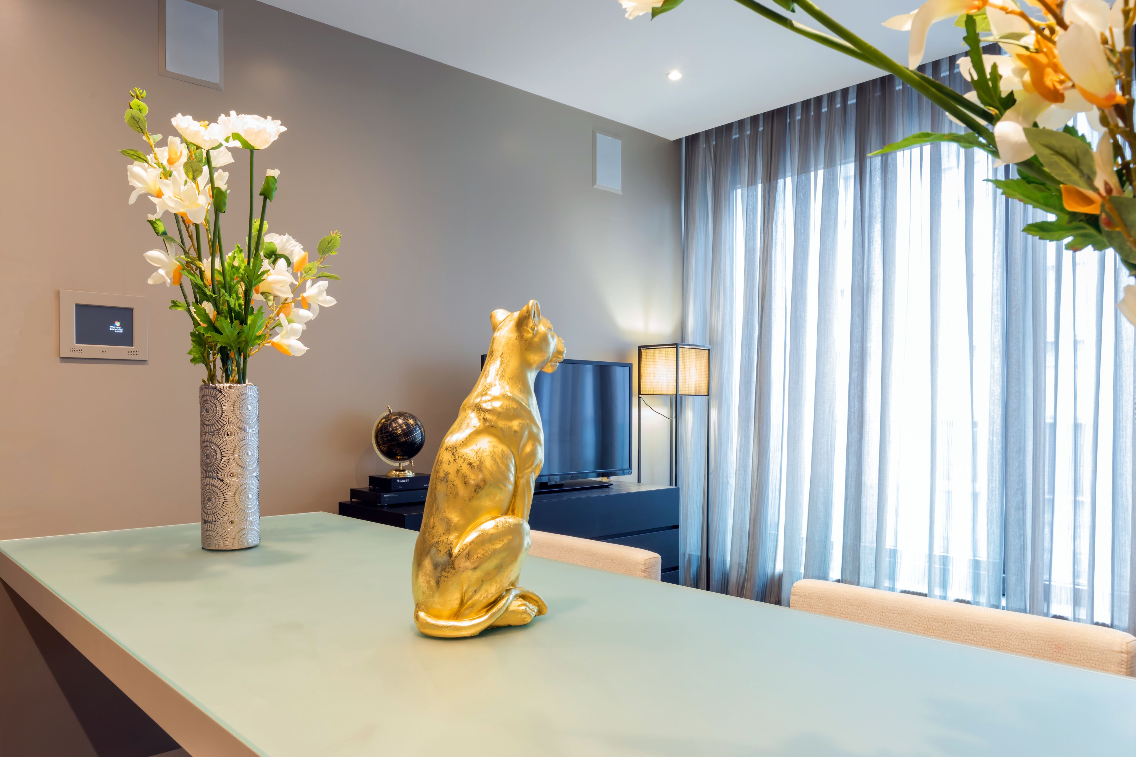 A modern living room with a sofa, a television, a decorative golden statue, and a vase of flowers.
