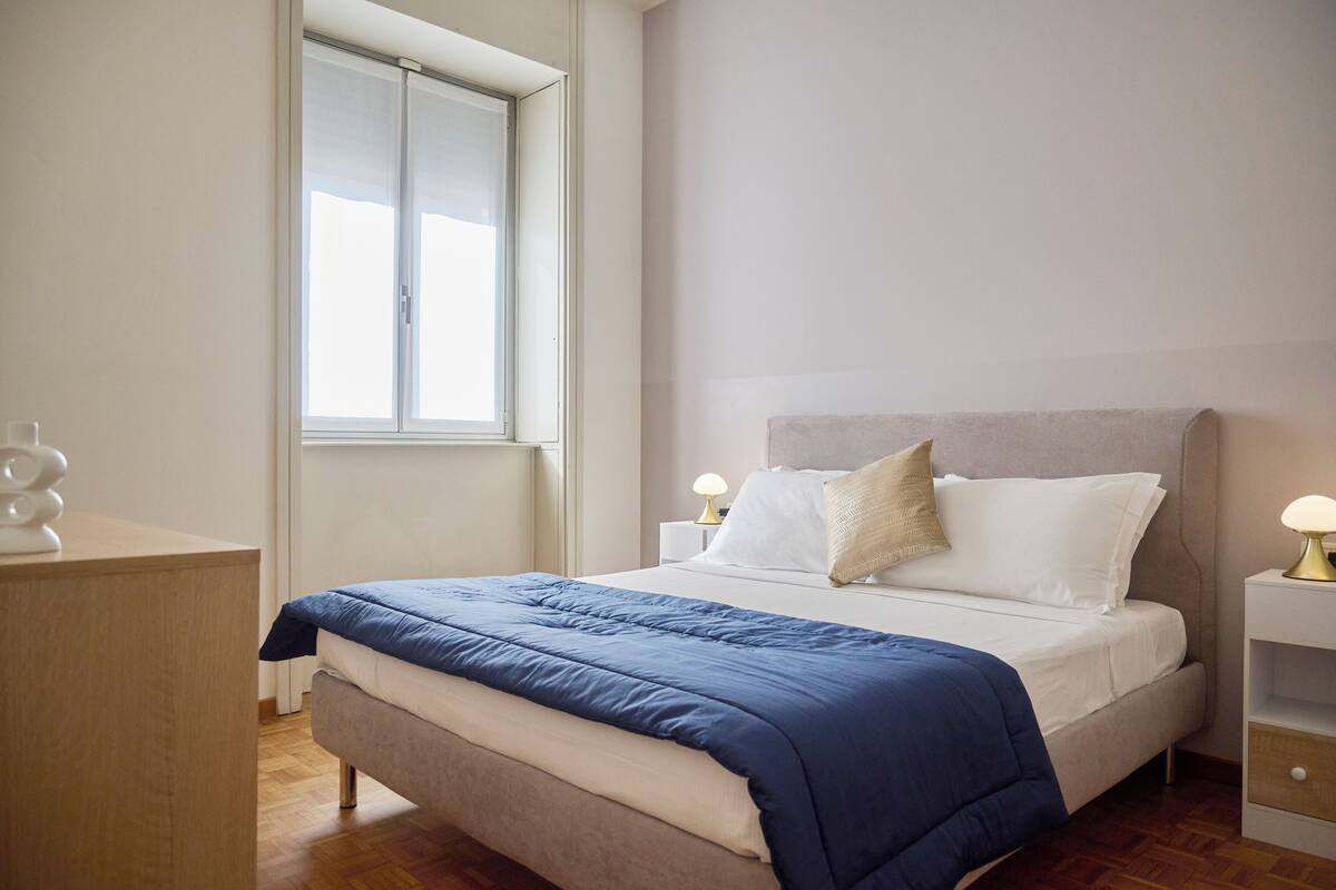 Un dormitorio con cama, mesitas de noche, una ventana y suelo de madera.