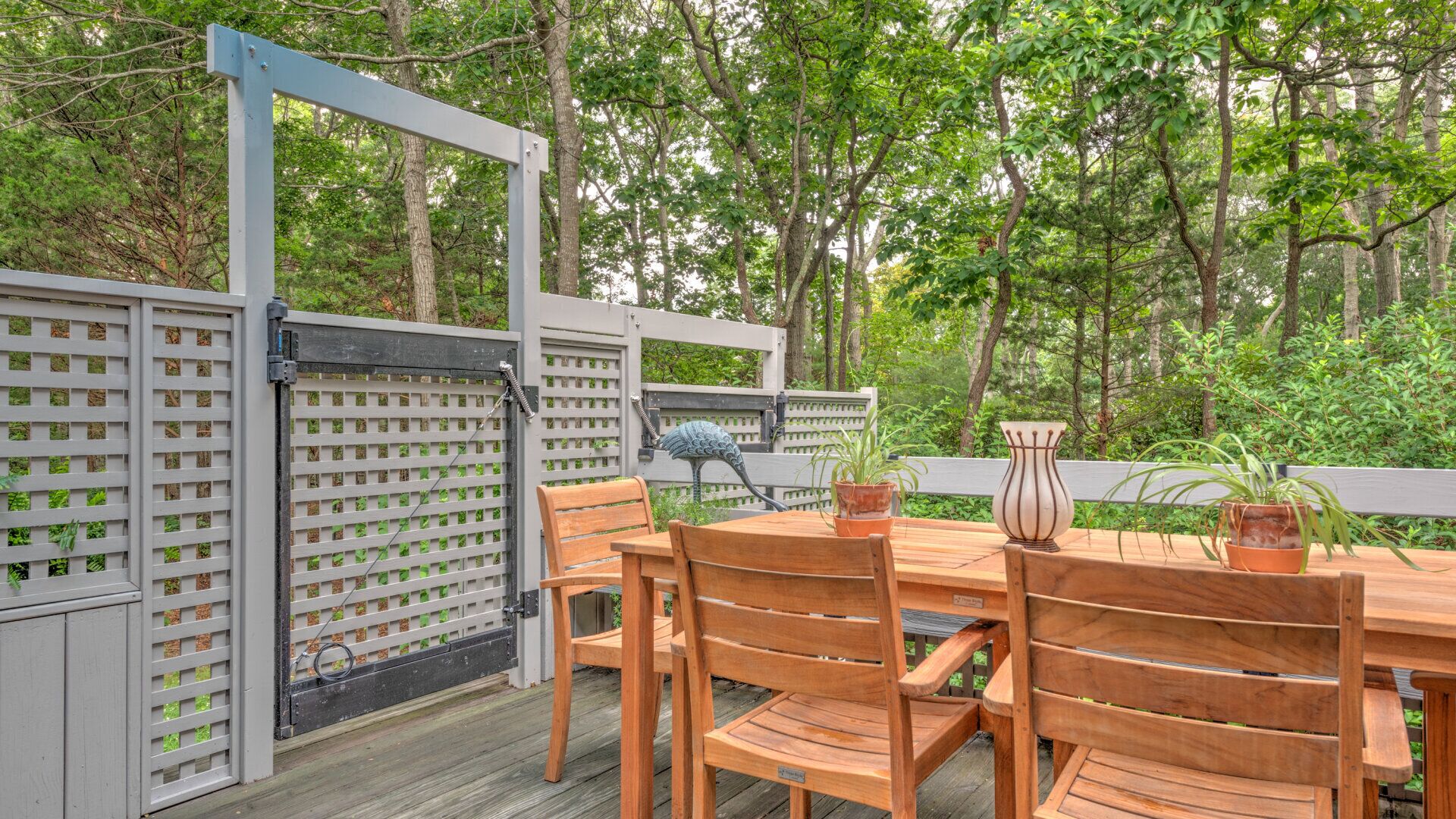 An outdoor wooden deck with a table and chairs, surrounded by a white fence with a lattice design.
