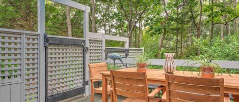 An outdoor wooden deck with a table and chairs, surrounded by a white fence with a lattice design.