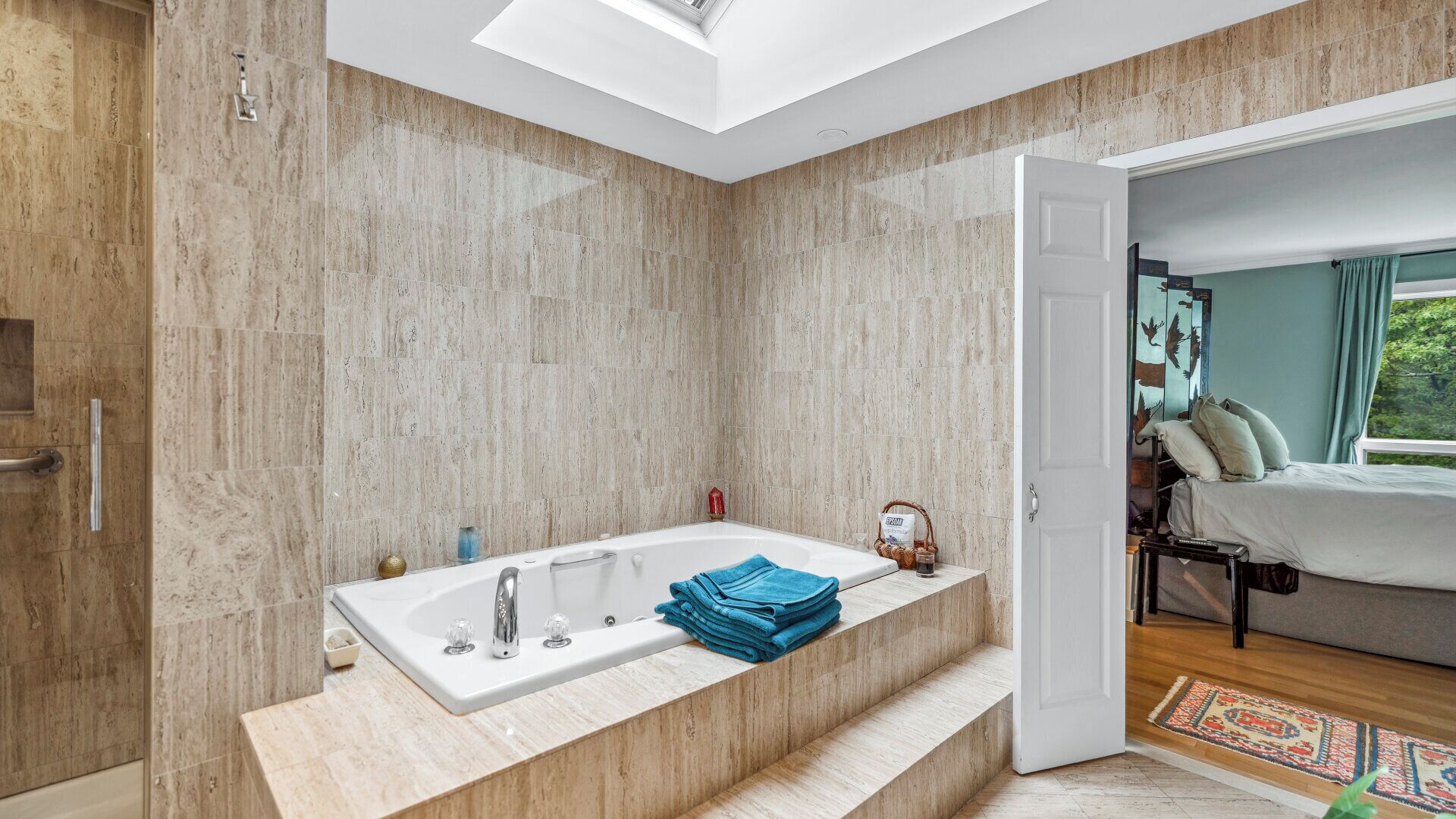 A modern bathroom with a freestanding bathtub, a skylight, and a view of a bedroom with a bed and a window.
