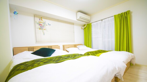 A hotel room with a large bed, two pillows, a window with blinds, a wall-mounted air conditioner, and a curtain. - Grande Shagi GS206 (Osaka)