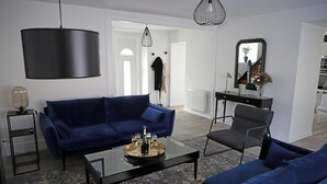 A modern living room with a blue sofa set, a coffee table with a tray of glasses, a black chair, and a black lamp. - La Belle Tuilière: A Charming Home in Champagne.  (Vandières)