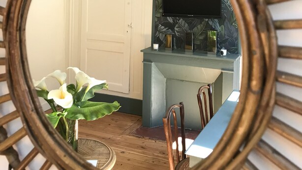 Un coin repas agrémenté d’un grand miroir rond qui reflète une pièce comprenant une porte, une table, des chaises, une plante et un téléviseur fixé au mur.