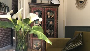 Un salon avec un canapé vert, un meuble décoratif orné de sculptures, un vase de fleurs blanches et une table ronde en bois.