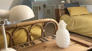 Une chambre mansardée chaleureuse avec un plafond en pente, une table en bois, une lampe, un lit recouvert d’une couverture verte et un objet décoratif blanc posé sur la table.