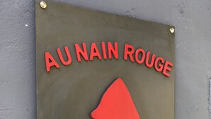 Une enseigne avec les inscriptions « AU NAIN ROUGE » et « GÎTE VINTAGE » sur un panneau métallique.
