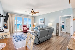 Ein Wohnzimmer mit grauem Sofa, einem roten Sessel, einem Deckenventilator und Meerblick durch große Schiebetüren.