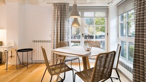 Un comedor con una mesa redonda, sillas de mimbre, una lámpara colgante y vistas amplias a través de grandes ventanales.