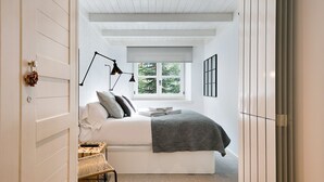 Un dormitorio con cama, mesita de noche, lámpara, ventana y vistas al exterior.