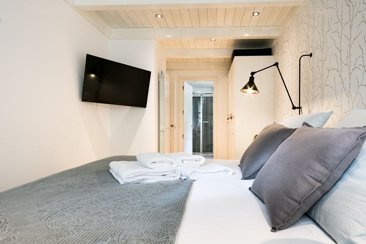 Habitación de hotel moderna con cama, televisor de pantalla plana, lámpara de noche y vista al baño por una puerta abierta.