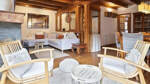 A cozy living room with a stone fireplace, wooden beams, a sofa, and wicker chairs. - Luderna - Apartamento con terraza Orri A3 (Gessa)