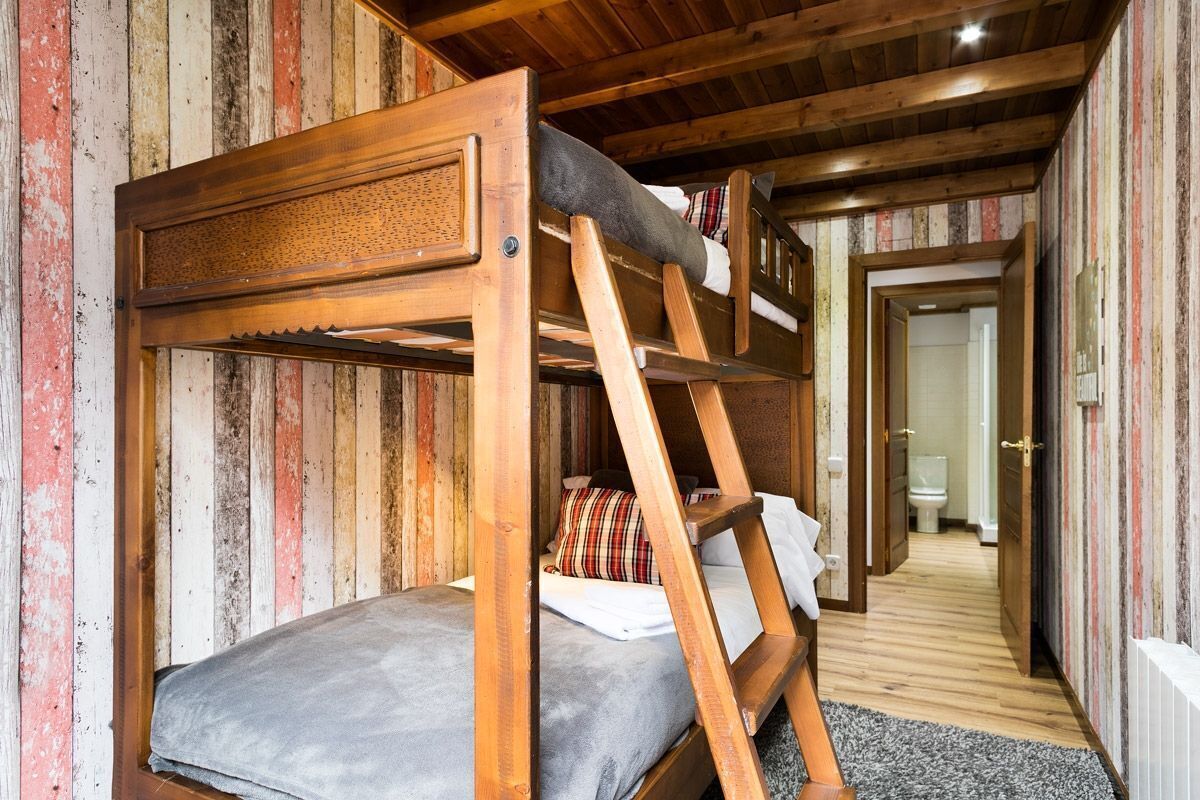 Una cama litera con escalera, paredes de madera y un pasillo que lleva a un baño.