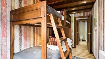 Una cama litera con escalera, paredes de madera y un pasillo que lleva a un baño.