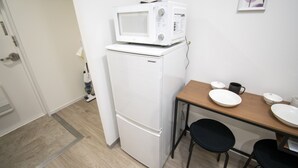 A compact kitchen with a white refrigerator, a microwave on top, and a small dining table with two black chairs. - Grande Shagi GS305 (Osaka)