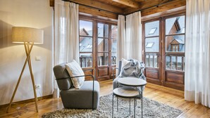 Una habitación acogedora con techo de madera, un sofá, una pequeña mesa redonda y ventanas amplias con cortinas.