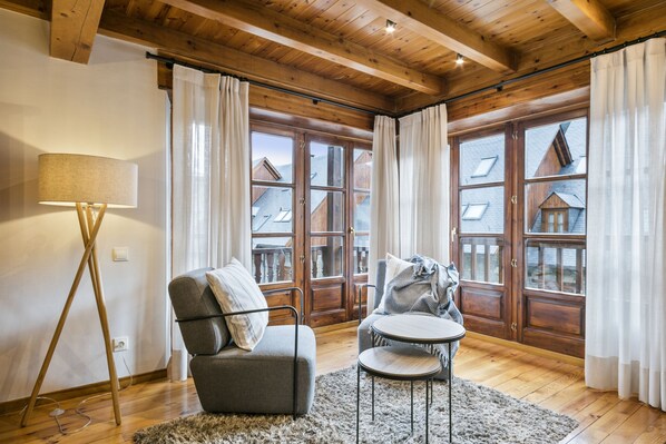 Um quarto aconchegante com teto de madeira, um sofá, uma mesa redonda pequena e grandes janelas com cortinas.