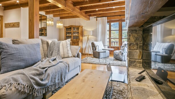 Un salón acogedor con techo de madera, chimenea de piedra y vistas al exterior.