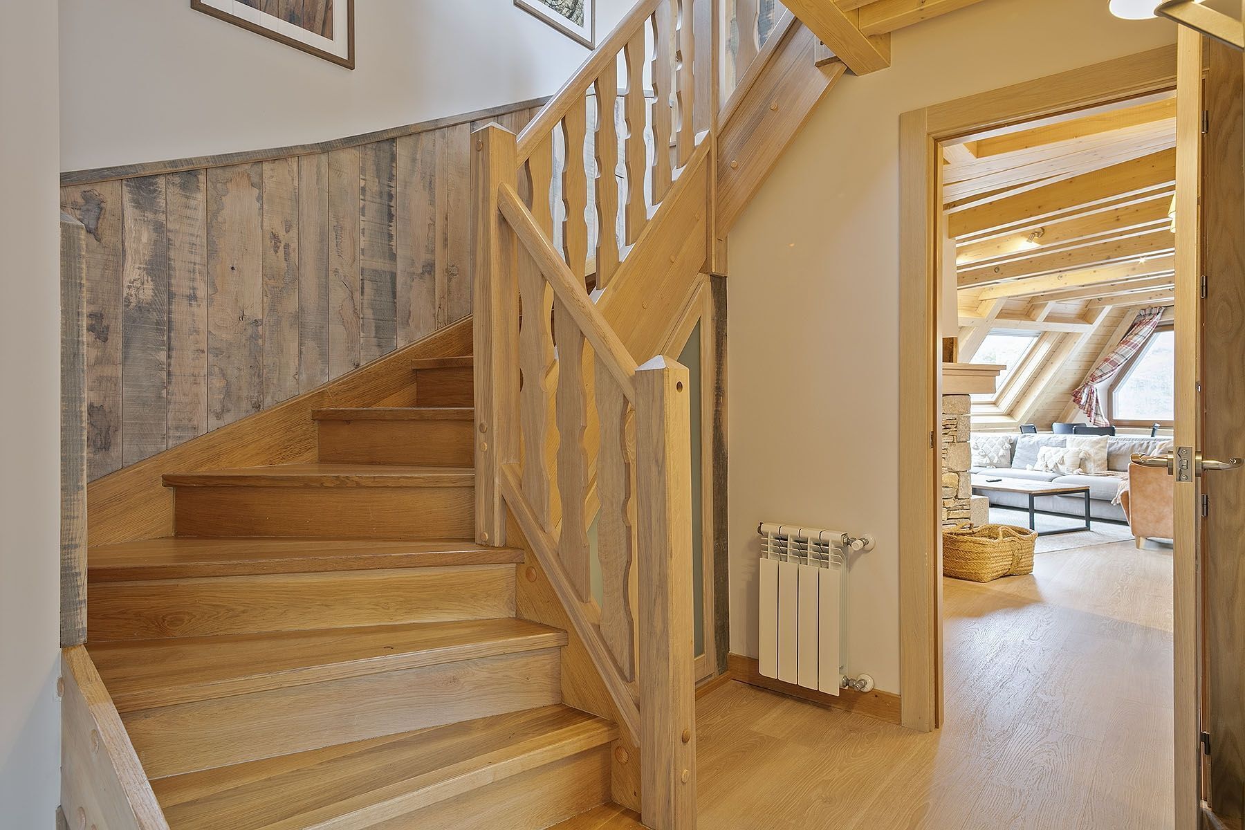 Eine Holztreppe mit Handlauf, die zu einem Raum mit Schrägdach und einer Couch führt.
