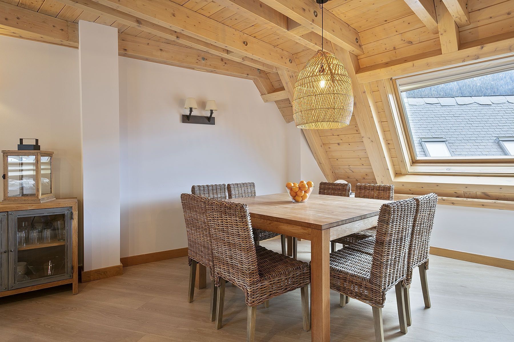 Een eetruimte met een houten tafel, rieten stoelen, een glazen kast en een hanglamp.
